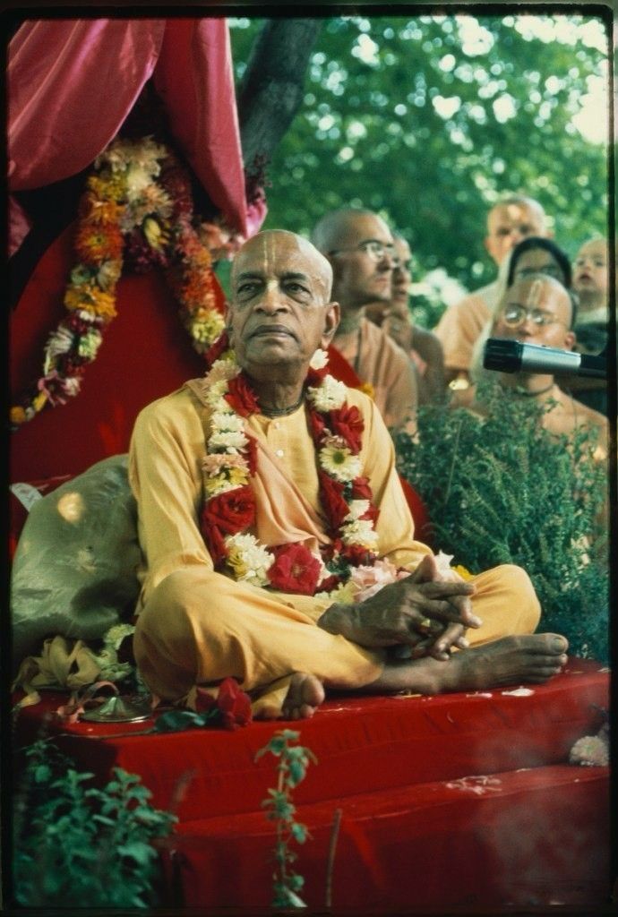His Divine Grace A.C. Bhaktivedanta Swami Prabhupada seated on a vyasasana in saffron robes, adorned with flower garlands